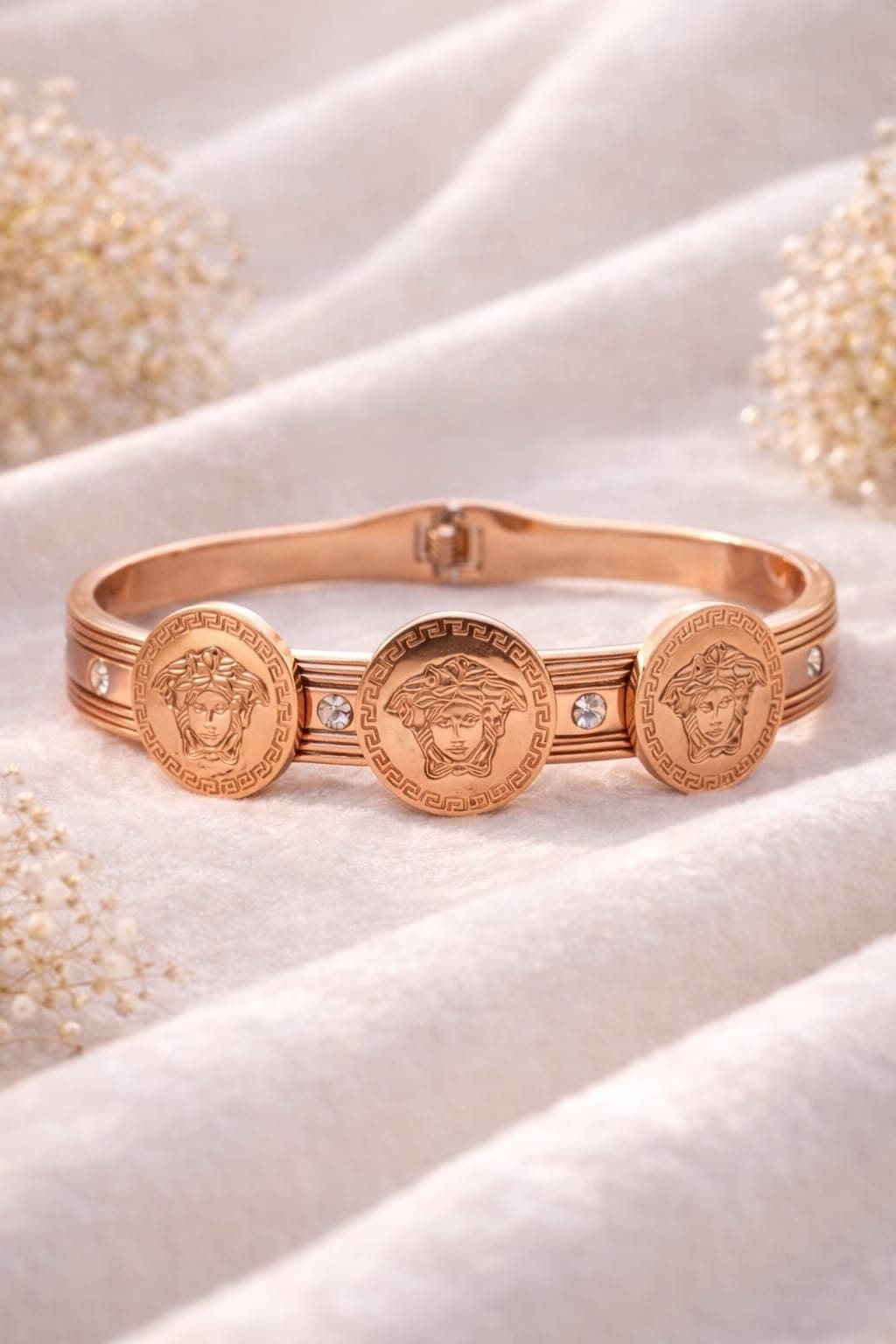 STRIKING ROSE GOLD  TONE FINISH ACCENTED WITH SIGNATURE  MEDUSA COIN MEDALLIONS, CRYSTAL EMBELLISHMENTS AND A CONVENIENT HINGED CLOSURE.